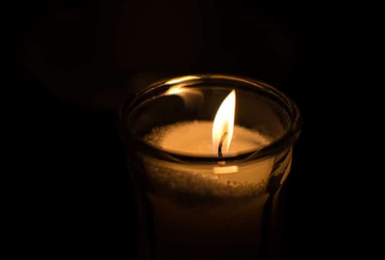 A single, softly lit candle with a focus on its flame, symbolizing remembrance and honoring a loved one.