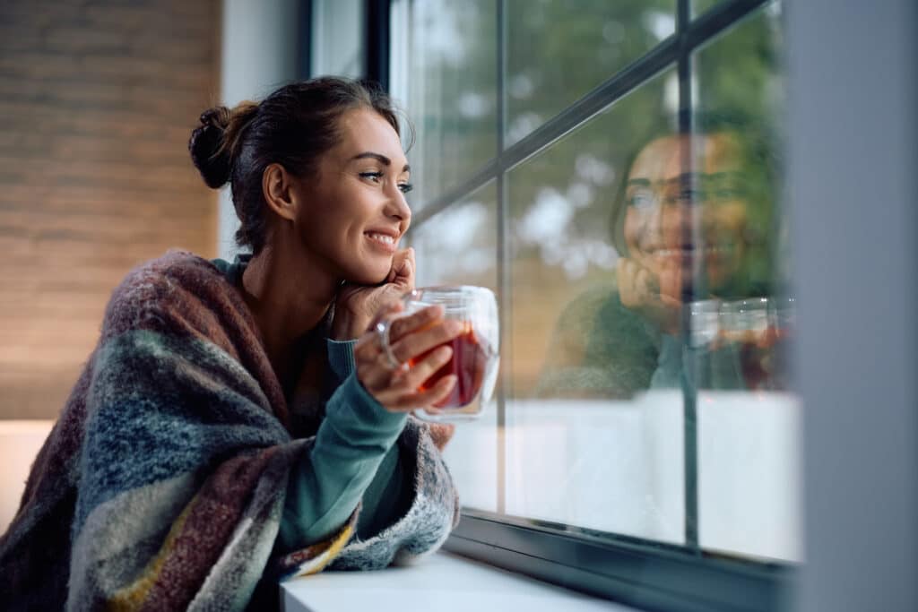 Woman wrapped in a blanket drinking tea, symbolizing holiday self-care and quiet reflection.